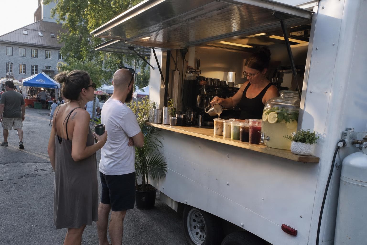 Une barista verse un café glacé à côté d'une limonade fraîche, dans un marché